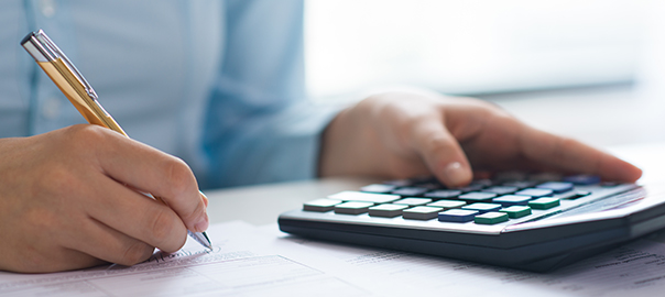 Closeup of person signing document and using calculator